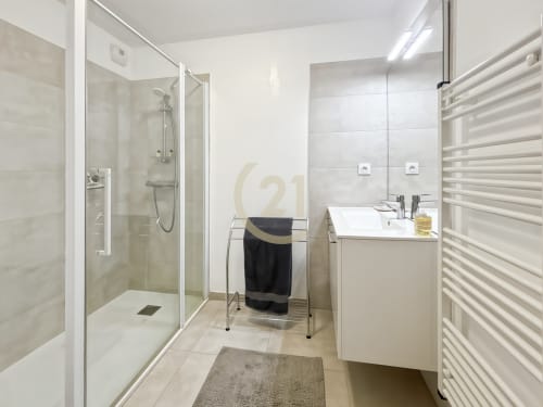 Salle de bain moderne de l'appartement de Calvi avec douche à l'italienne, vasque blanche, sèche-serviettes chauffant et carrelage en marbre