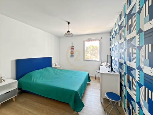 Chambre moderne dans un appartement de Calvi avec tête de lit bleu, literie turquoise, mur d'accent géométrique et vue sur la ville