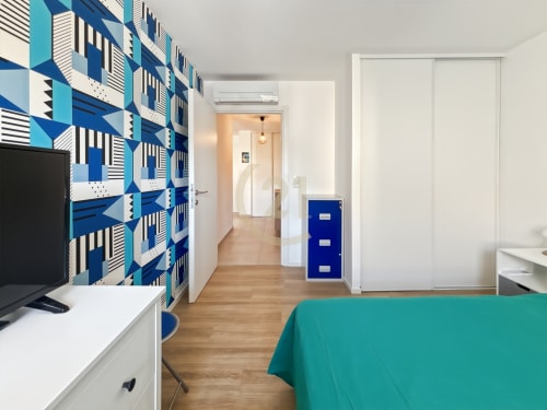Chambre moderne d'appartement à Calvi avec papier peint géométrique bleu, bureau TV, lit turquoise et parquet