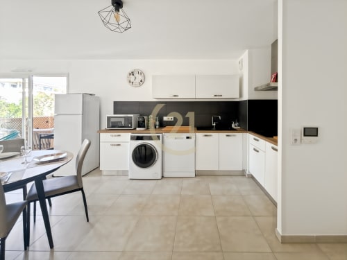 Cuisine moderne avec armoires blanches, dosseret noir et coin repas dans un appartement à Calvi