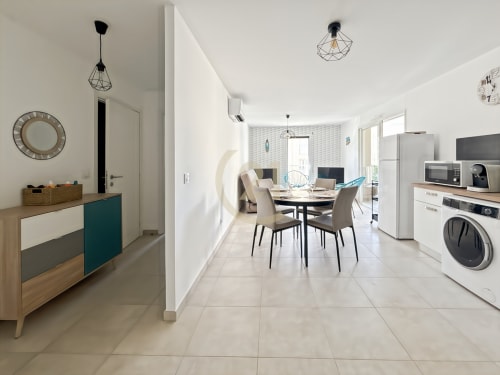 Appartement moderne ouvert à Calvi avec table à manger, cuisine, lave-linge et vue sur la ville par les portes de la terrasse