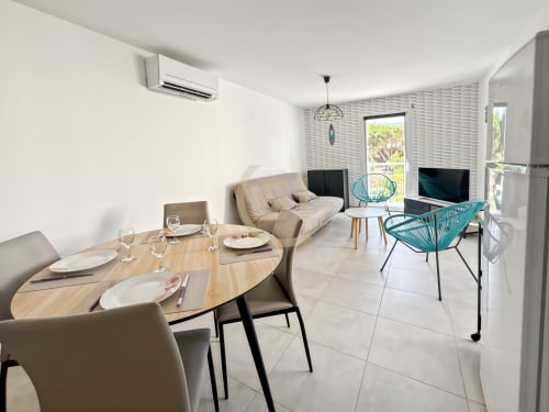 Séjour moderne à Calvi avec table à manger, canapé beige, télévision, chaises turquoise et accès à la terrasse