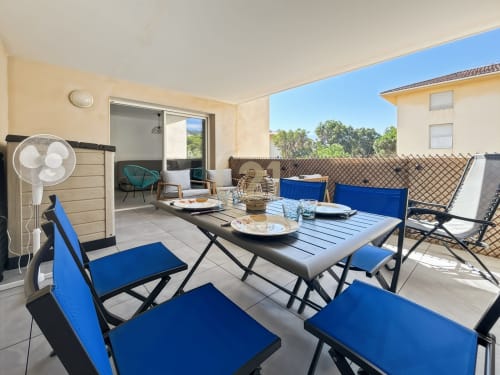 Terrasse spacieuse avec table de salle à manger, chaises bleues et vue sur la mer, appartement à Calvi