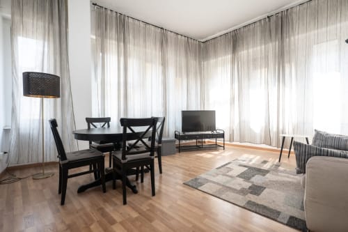 Luminoso appartamento Milano Duomo con mobili da pranzo neri, TV, pavimenti in legno e tende leggere che lasciano filtrare la luce naturale