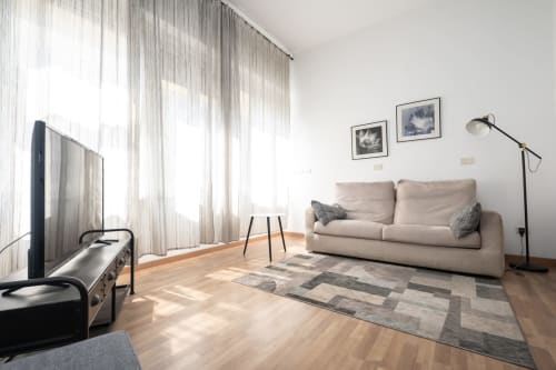 Luminoso salotto milanese con divano beige, pavimenti in legno, TV e luce naturale dalle ampie vetrate