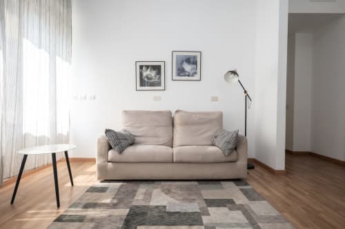 Luminoso soggiorno di appartamento milanese con divano beige, lampada da terra moderna, arte botanica incorniciata e tappeto geometrico