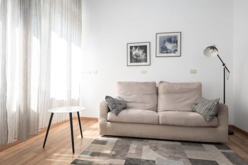 Soggiorno moderno a Milano con divano beige, tappeto geometrico, quadri incorniciati, tavolino laterale e lampada da terra vicino alla finestra