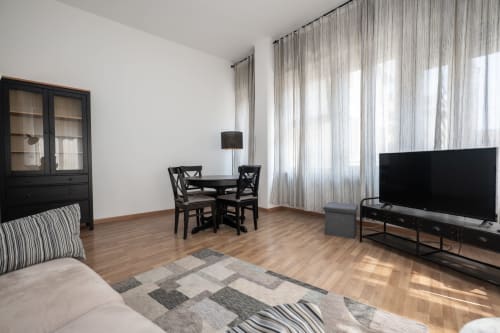 Appartamento moderno a Milano con letto, zona pranzo, TV e finestre a tutta altezza che inondano di luce naturale