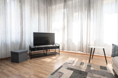 Luminoso soggiorno moderno nell'appartamento Duomo Home di Milano con TV, parquet, tappeto geometrico e finestre a tutta altezza