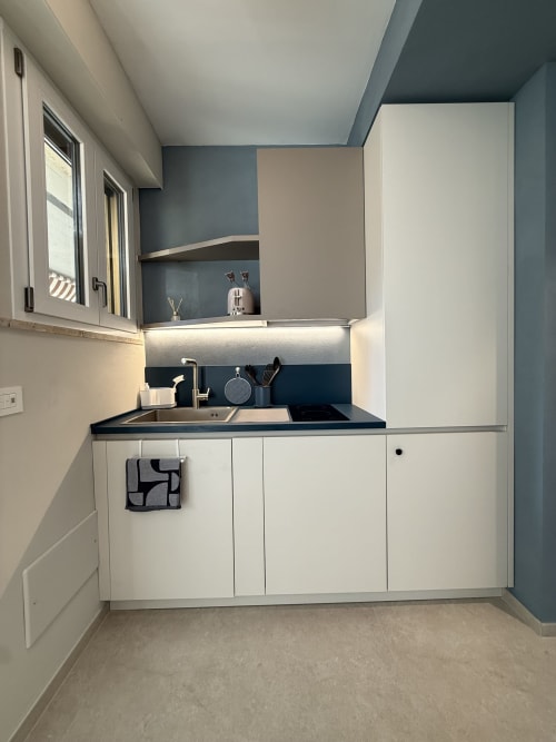 Kitchenette moderna con mobili bianchi, piano cottura nero e rivestimento blu-grigio nell'appartamento La Casetta dei Ronchi,