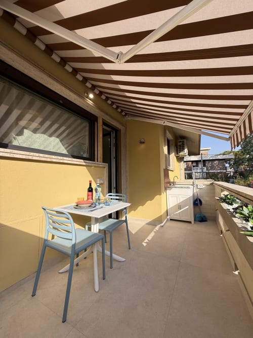 Terrazza soleggiata con tenda a righe a La Casetta dei Ronchi, Marina di Massa. Area pranzo con sedie blu vista mare
