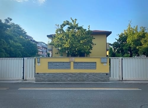 Casa gialla con cancellata bianca a La Casetta dei Ronchi, Marina di Massa, circondata da alberi sotto cielo azzurro