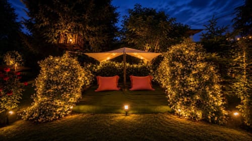 Giardino notturno di Gan Eden B&B con piante fiorite illuminate, sedute lounge e ombrellone a San Benedetto del Querceto