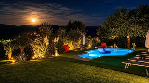 L'area piscina di Gan Eden al chiaro di luna con illuminazione paesaggistica, lettini e vista sulle colline toscane al tramonto
