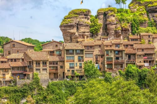 Historic stone buildings with terracotta roofs nestled below moss-covered cliffs in Susqueda, Girona