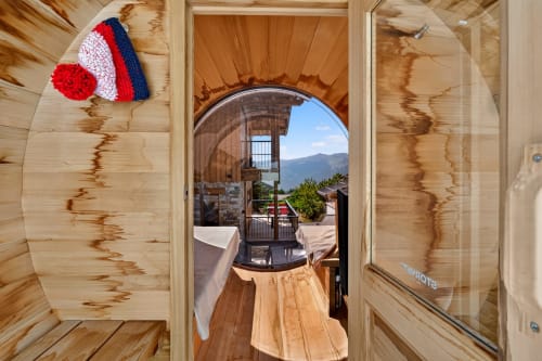 Cozy wooden chalet interior at L'Alp'In with mountain view through open door, striped knit hat decor