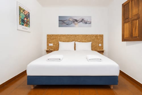 Quarto moderno na Quinta de Carvalhal em Guimarães com roupa de cama branca, cabeceira em cortiça e piso em azulejo de barro