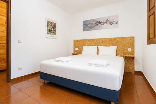 Quarto moderno na Quinta de Carvalhal com cabeceira em cortiça, roupa de cama branca, pavimento em terracota e vista para o jardim em Guimarães