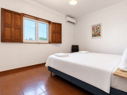 Quarto luminoso na Quinta de Carvalhal em Guimarães com cama branca, azulejos de terracota, janelas de madeira e vistas do jardim