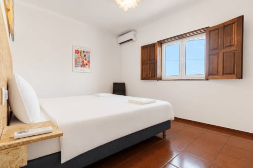 Quarto luminoso na Quinta de Carvalhal com cama branca, portadas de madeira, piso em terracota e vista para o jardim em Guimarães