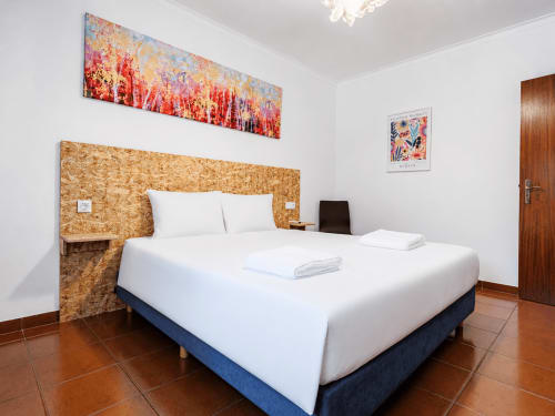 Quarto moderno na Quinta de Carvalhal em Guimarães com cabeceira de cortiça, roupa de cama branca e arte colorida na parede
