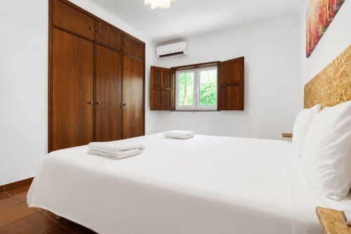 Quarto espaçoso na Quinta de Carvalhal em Guimarães com guarda-roupa em madeira, cama branca, janelas com vista para jardim e ar condicionado