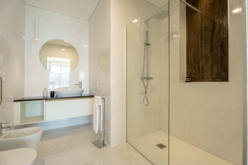 Modern bathroom at Suites Avenue Lux Apartments in Horta with rainfall shower, round mirror, and sleek vanity
