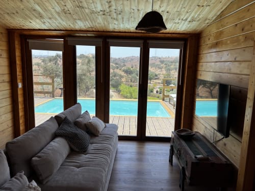 Sala de estar contemporânea com sofá cinzento com vista para piscina turquesa e paisagem rural de Almodôvar na villa Corvatos Casas do Monte