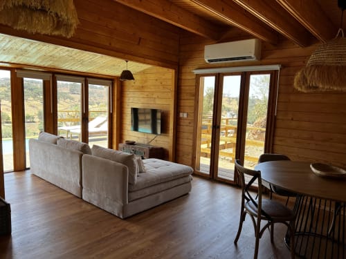 Sala de estar de villa de madeira moderna com sofá bege, TV, mesa de jantar e vistas panorâmicas das montanhas e piscina em Corvatos
