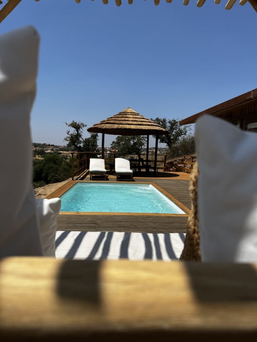 Piscina turquesa com deck de madeira, espreguiçadeiras sob gazebo com cobertura de palha e vista da zona rural na villa Casa do Montado