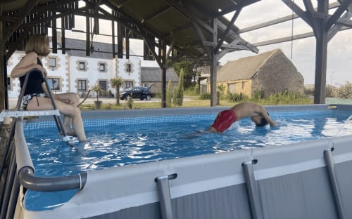 Guest swimming in outdoor pool at Ty Koant hotel in Cléder, France, with covered area and countryside views