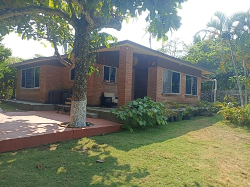 Villa Casa Flais en La Morada, Monte Gordo: fachada de ladrillo rojo, porche cubierto y jardín tropical exuberante