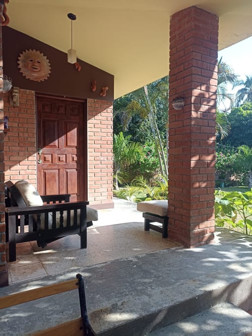 Porche de la villa Casa Flais con columnas de ladrillo, muebles negros y vista al jardín tropical del hotel La Morada, Monte Gordo, México