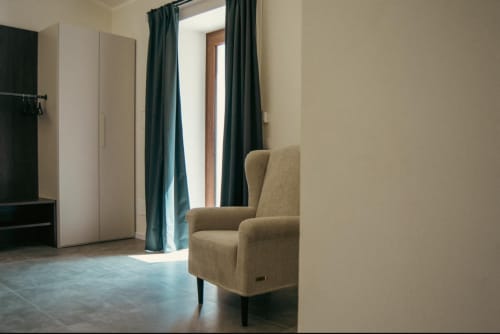 Camera moderna del Baglio Capo a Siculiana con poltrona beige, porta in legno e tende turchesi