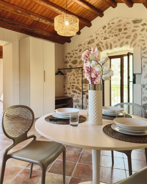 Elegante sala da pranzo al Baglio Capo con muri in pietra, tavolo rotondo bianco, sedie moderne e orchidee rosa a Siculiana, Sicilia.