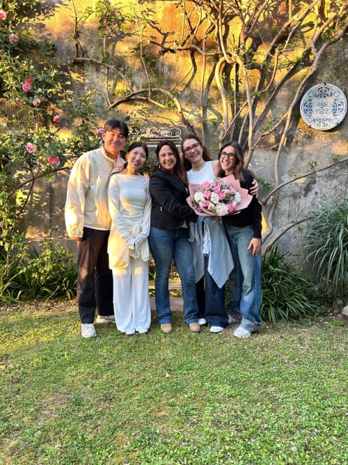 Cinque ospiti posano con fiori al Relais Palazzo Cacace a Meta di Sorrento, Italia, in un'ambientazione da giardino.