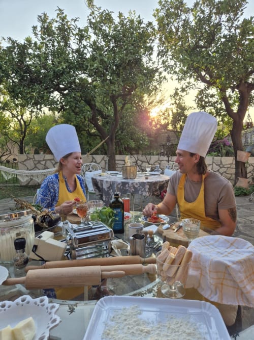 Due chef in grembiuli gialli e toque bianche preparano la pasta durante una lezione di cucina al tramonto nel giardino di Meta di Sorrento.