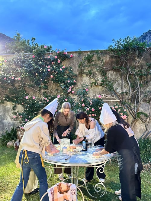 Gli ospiti si riuniscono intorno a un tavolo in giardino presso il Relais Palazzo Cacace, Meta di Sorrento, con rose rosa che si arrampicano sul muro di pietra