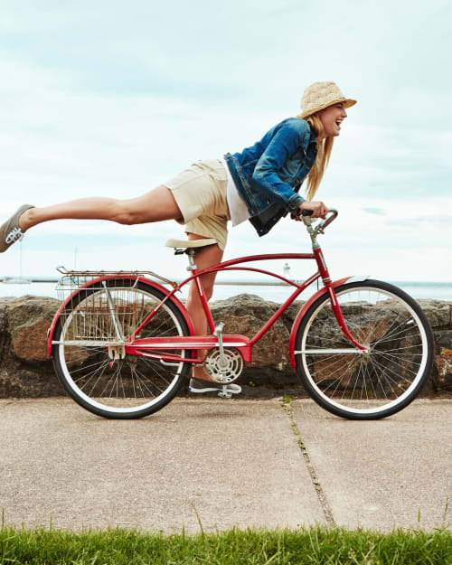 Donna che posa giocosamente su una bicicletta vintage rossa in una spiaggia costiera italiana