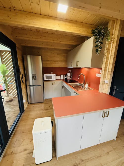 Cuisine moderne de la villa AZALÉE avec dosseret orange, armoires blanches, îlot central et poutres en bois