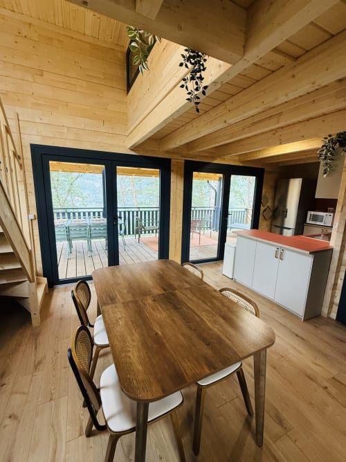 Salle à manger moderne du Lodge AZALÉE aux Cabanes et lodges du Belvédère avec table en bois et portes vitrées noires vue sur le lac
