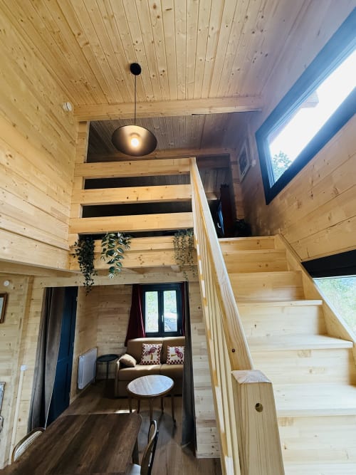 Intérieur de lodge en bois moderne avec escalier, plantes suspendues, luminaire suspendu et coin détente à Serrières-sur-Ain