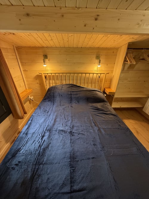 Chambre chaleureuse en bois avec literie bleue, tête de lit métallique et éclairage chaleureux aux Cabanes du Belvédère, Serrières-sur-Ain