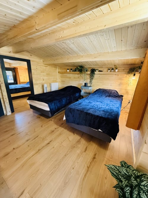 Chambre spacieuse du lodge en bois avec deux lits, literie bleue, poutres apparentes et vue sur les montagnes aux Cabanes Belvédère