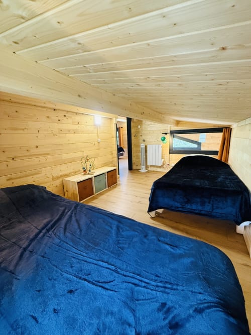 Chambre spacieuse en bois avec trois lits et literie bleue, vue sur le lac et les montagnes aux Cabanes et lodges du