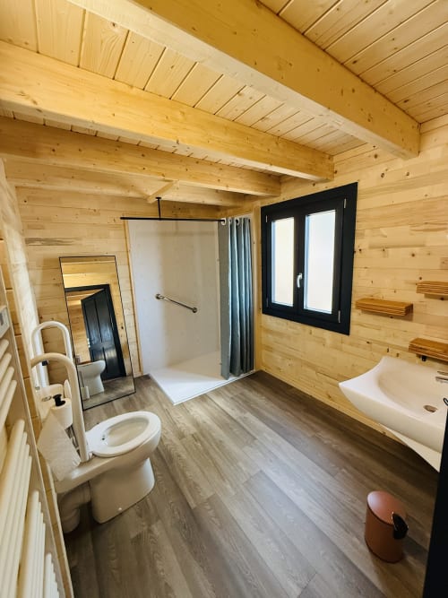Salle de bains rustique en bois avec toilettes, lavabo, douche et fenêtre aux cadres noirs au Belvédère