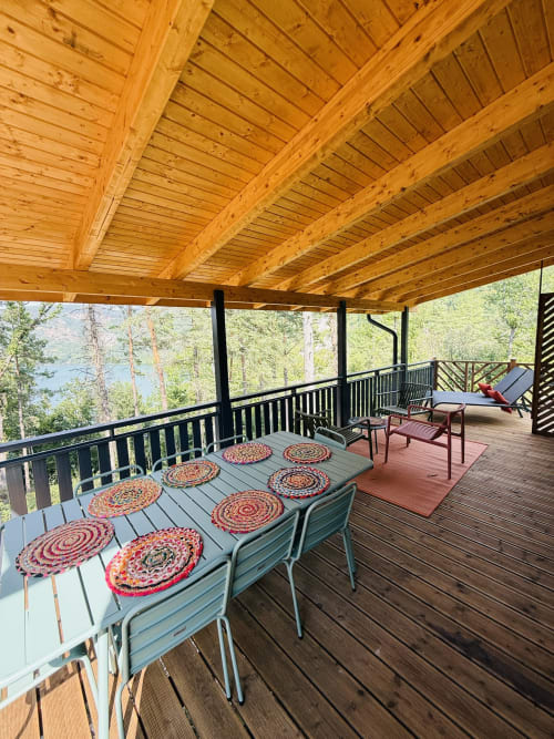 Terrasse couverte du Lodge AZALÉE avec table à manger, coussins colorés, vue sur le lac, forêt et rampes métalliques