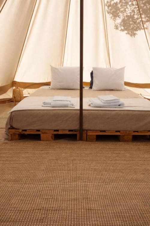 Interior da tenda glamping em Monte da Tojeirinha com camas espelhadas, almofadas brancas, estruturas de paletes de madeira e vistas para o lago