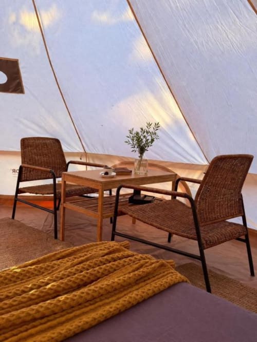 Interior da tenda glamping em Monte da Tojeirinha com cadeiras de vime, mesa de madeira e vista para o lago através das paredes de lona