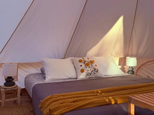 Interior de tenda luxuosa na Monte da Tojeirinha com cama, almofadas, iluminação aconchegante e vista para o lago em Montargil, Portugal